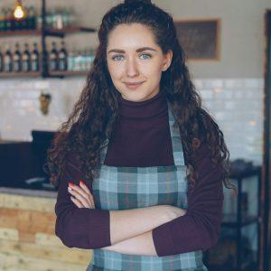 Dueña de un local de comida sonriendo con los brazos cruzados detrás de su mostrador