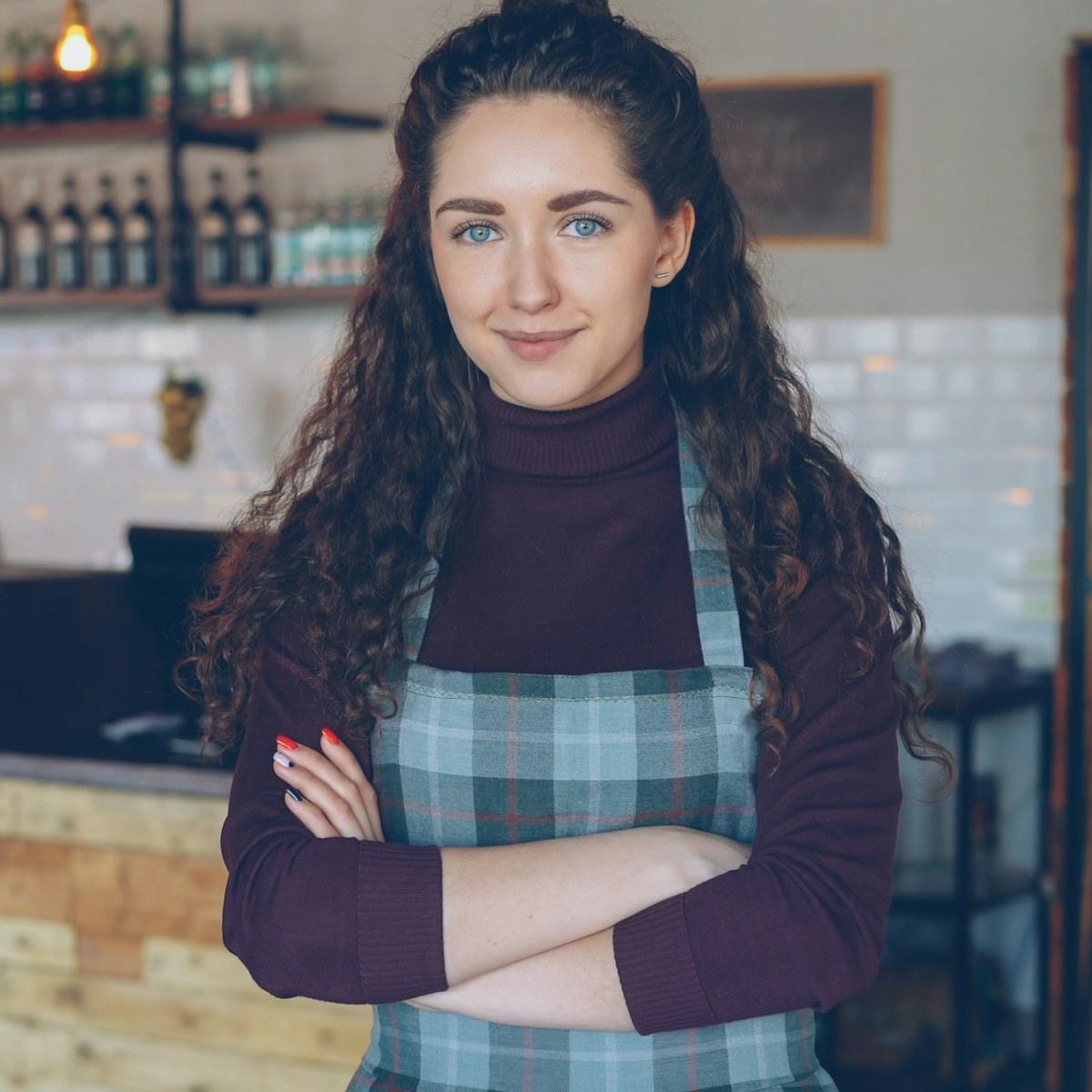 Dueña de un local de comida sonriendo con los brazos cruzados detrás de su mostrador
